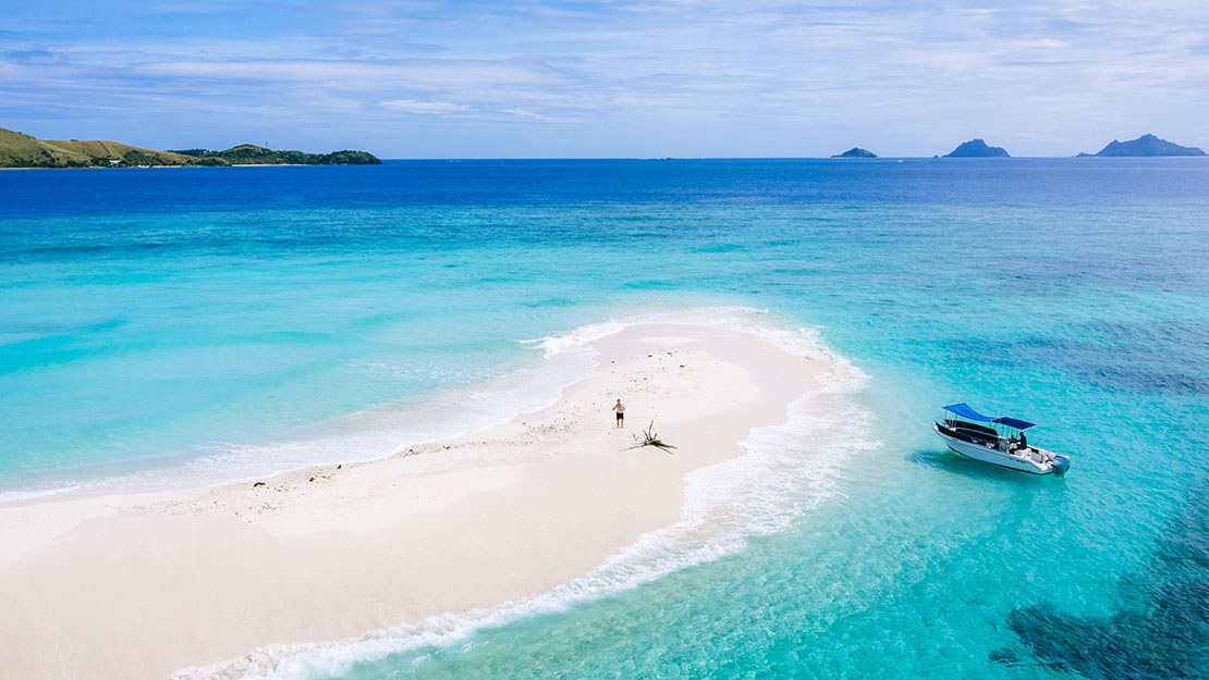 A remote sand cay in Fiji's Mamanuca Islands, a single figure on the white sandbar with clear blue water